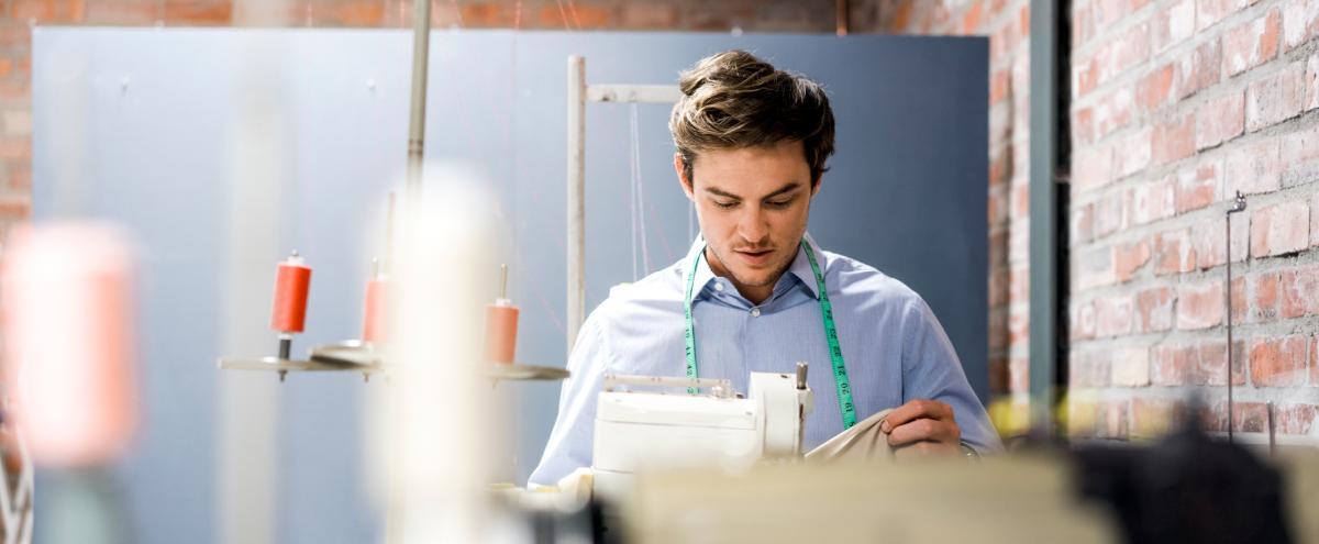 foto van een man in een naaiatelier die geconcentreerd met stof in de weer is