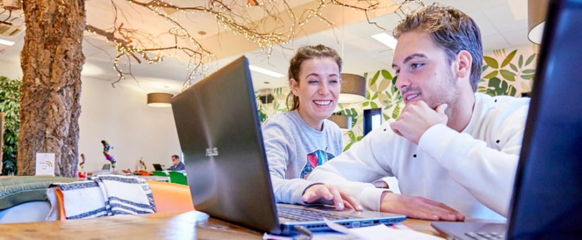 Foto van een jongen en een meisje die lachend achter een laptop zitten