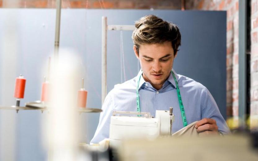 foto van een man in een naaiatelier die geconcentreerd met stof in de weer is