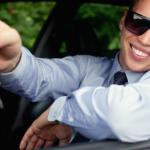 Foto van een lachende jongeman achter het stuur van een auto met een autosleutel in zijn hand